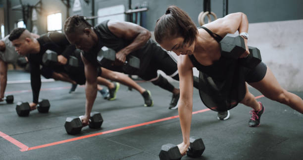 shot of a group of sporty young people doing pushups and renegade rows together in a gym